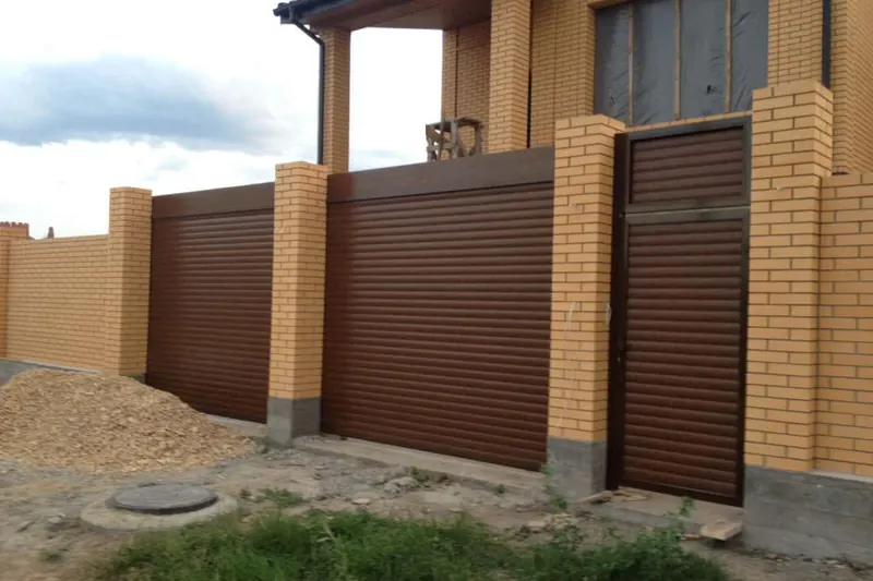 Ролетні ворота коричневого кольору в цегляній огорожі