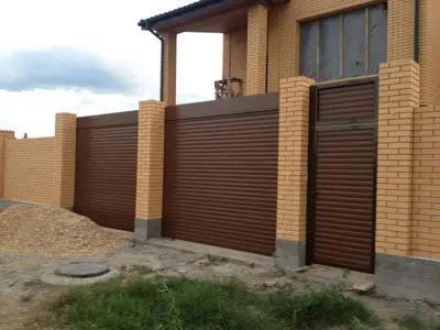 Коричневі ролети на вікнах будинку за цегляним парканом